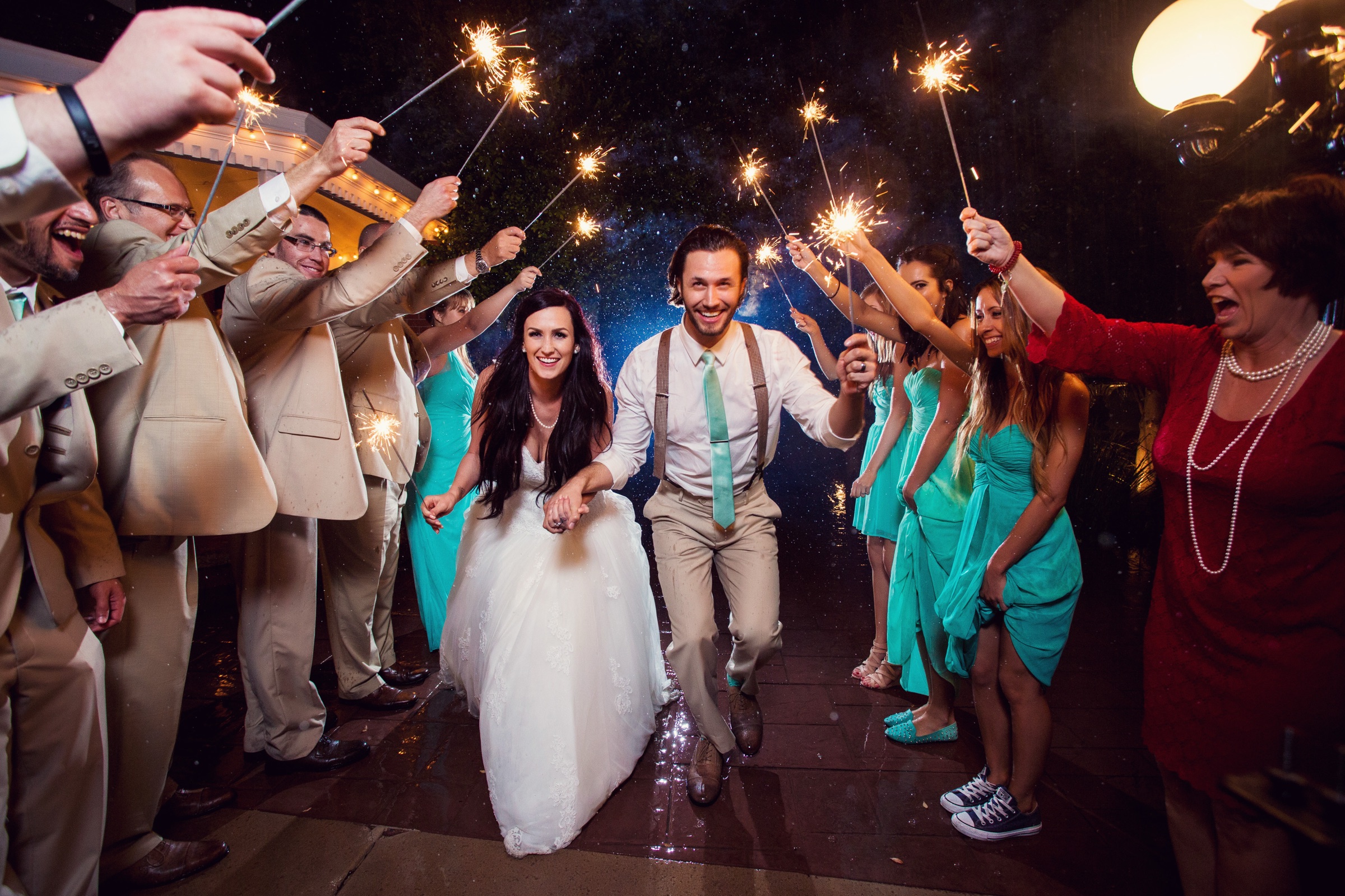 Couple walking through sparklers with wedding guests cheering