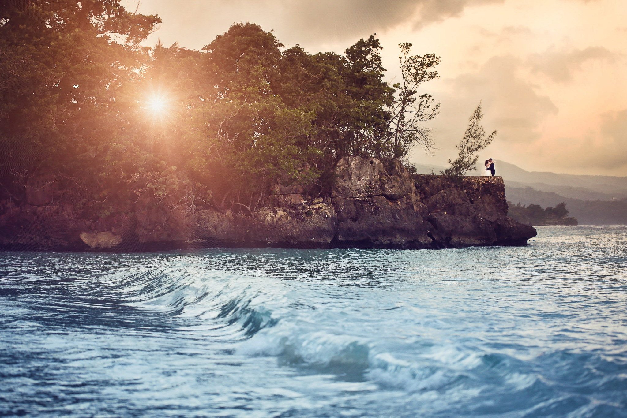 Couple standing together on a cliff at sunset